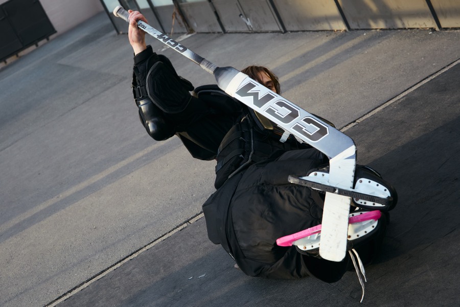 Marks rolling back on the rink floor with a hockey stick across his raised legs